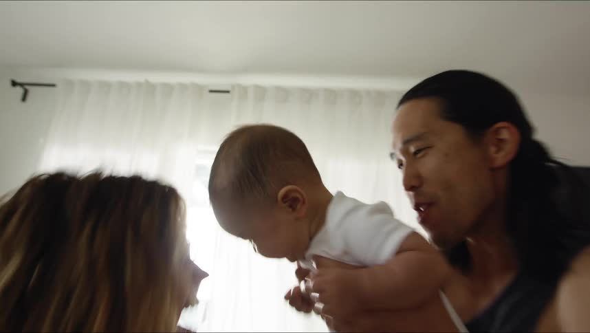 Father with black undershirt holds baby and dances with mother with brown wavy hair in living room at home