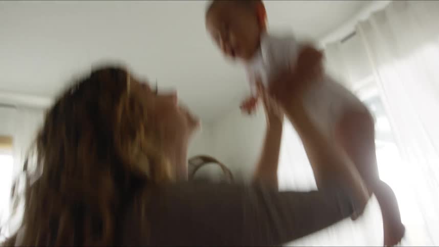 Mother dancing and lifting baby up and down in the living room