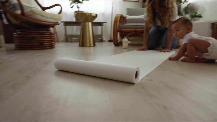 A woman rolls out butcher paper on her living room floor as her baby watches