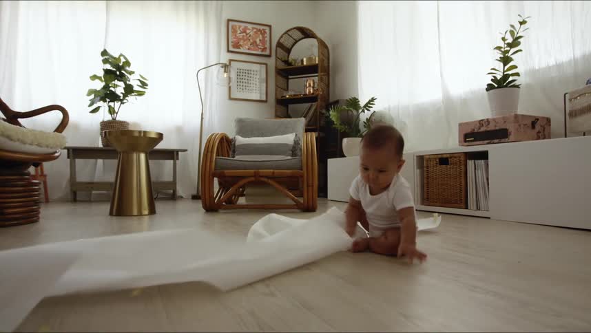 A small infant plays on the floor with a roll of paper towels