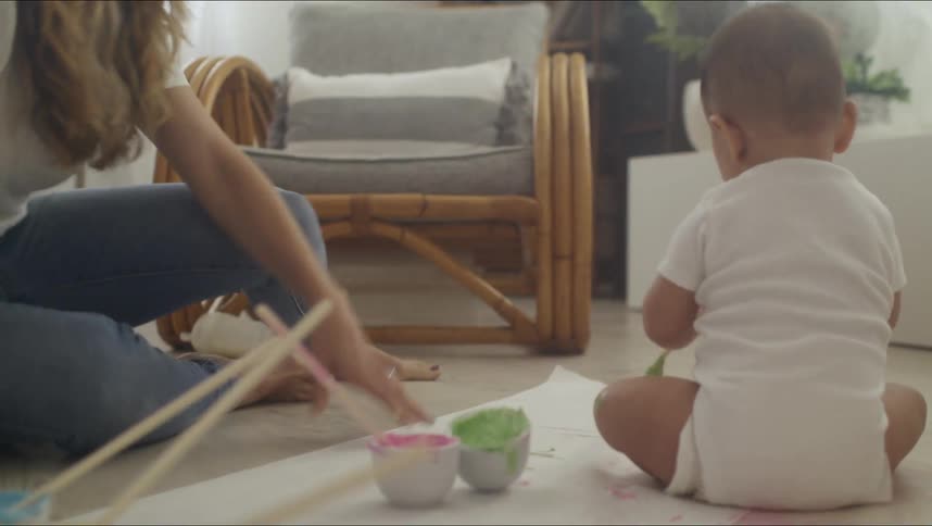 Mom tries to help when a messy baby puts a paint brush in his mouth