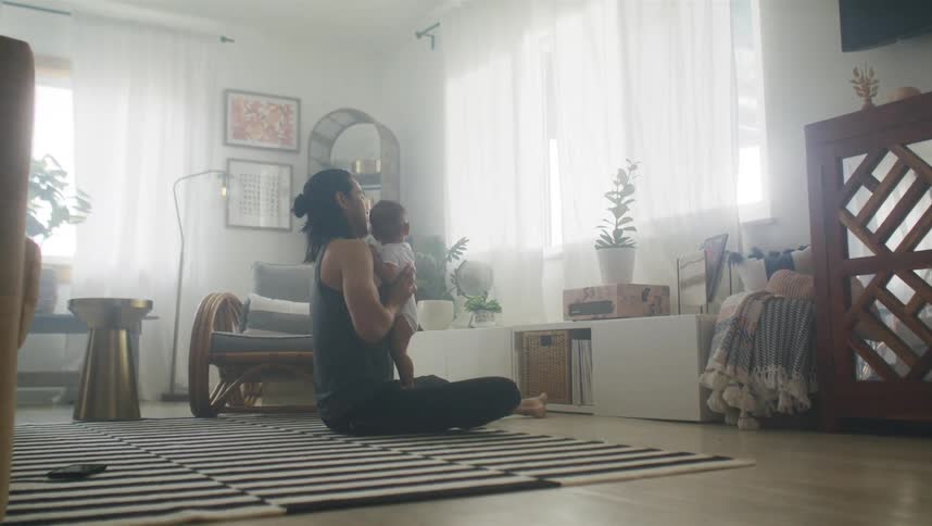 Mother holding and kissing her baby while sitting at the carpet in the middle of the living room