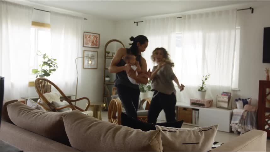 A woman dances toward her partner and baby as they play in the living room