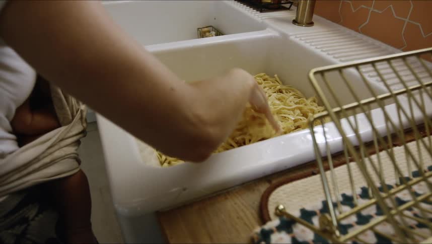 Woman stirs home made pasta with her hand in a sink
