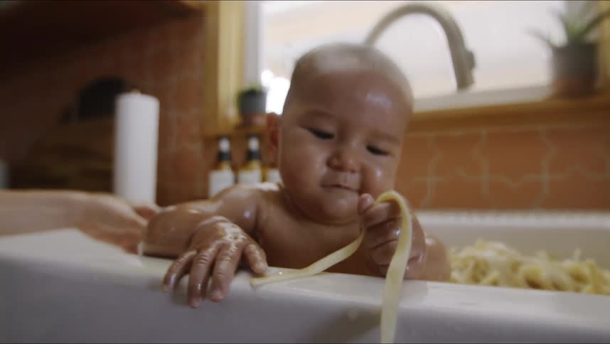 A baby is playing in a sink of pasta