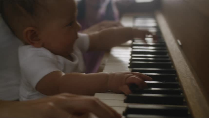 Mother with white t shirt holds baby son playing piano