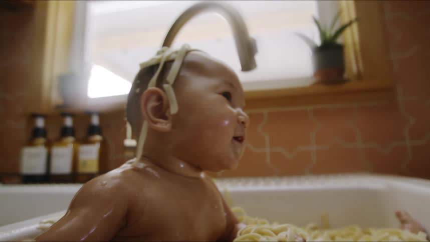 An infant plays with pasta in a kitchen sink