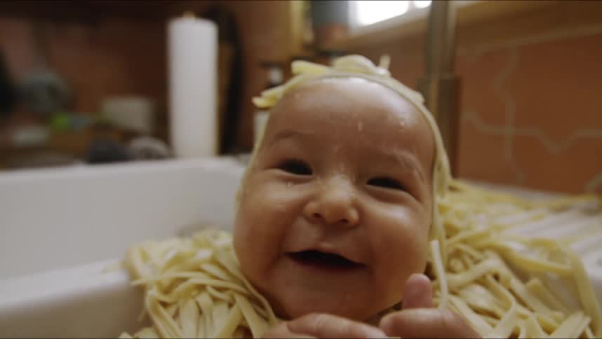 Baby covered in noodles sits in kitchen sink smiling