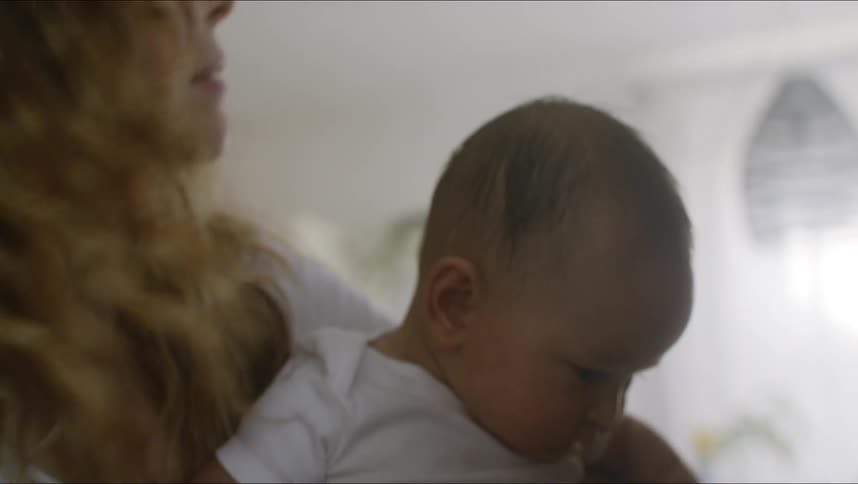 Mother with brown wavy hair and white shirt holds baby son at home