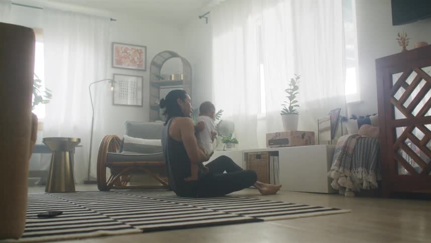 A man rocks his infant son up and down while sitting on the floor of their living room