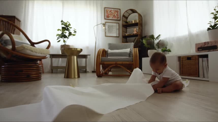 A baby pulls on a roll of paper while sitting on the floor