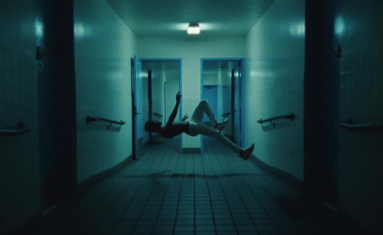 Man floats over tiled floor in corridor lined by handle bars
