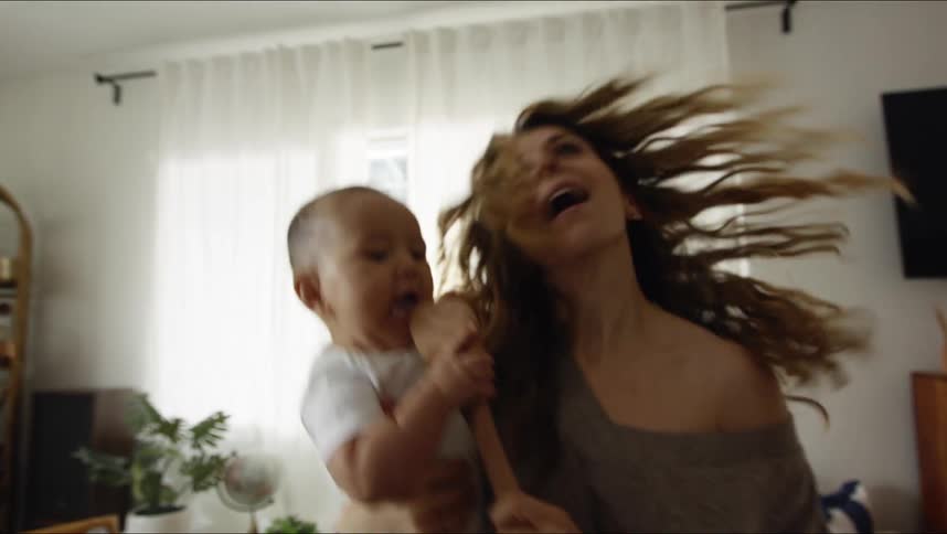A woman uses a wooden spatula as a microphone while singing and dancing with her baby