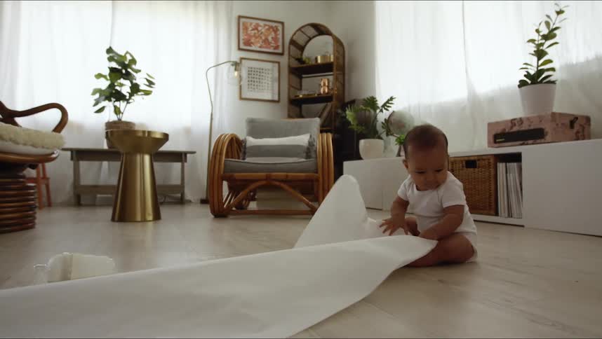 Baby sitting on hardwood flooring playing with a roll of butcher paper