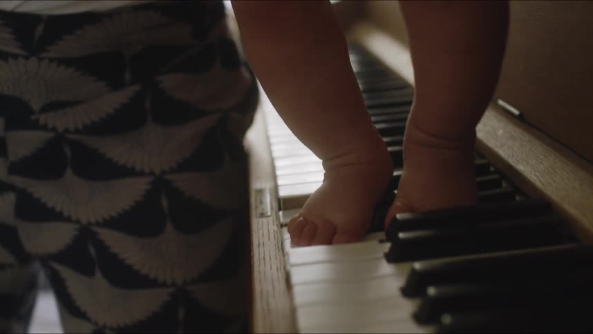 Babys toes jump and walk on piano keys as a parent carries them across