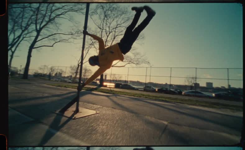 A man in a park jumps and grabs on to a pole and hangs sideways on the pole