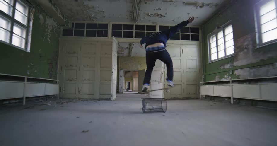 A young man attempts to jump over a trash bin on a skateboard but falls off