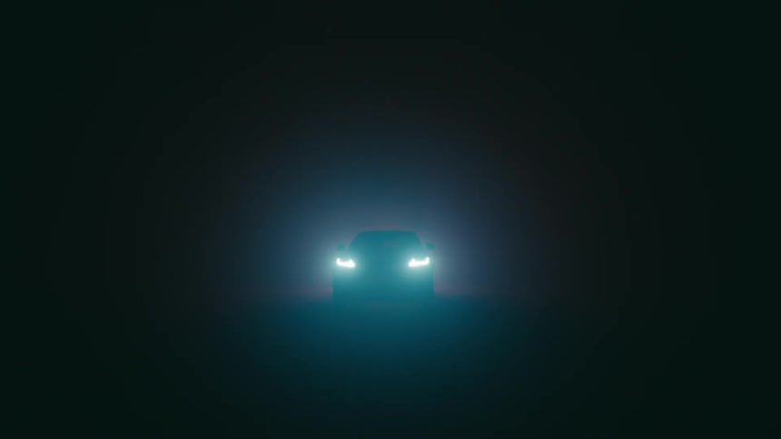 An automobile is sitting in the darkness and turns on the headlights
