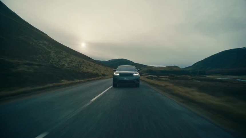 A car drives down a street past rolling hills