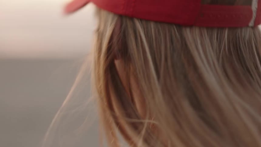 Blonde woman wearing a red cap bobbing her head on the beach