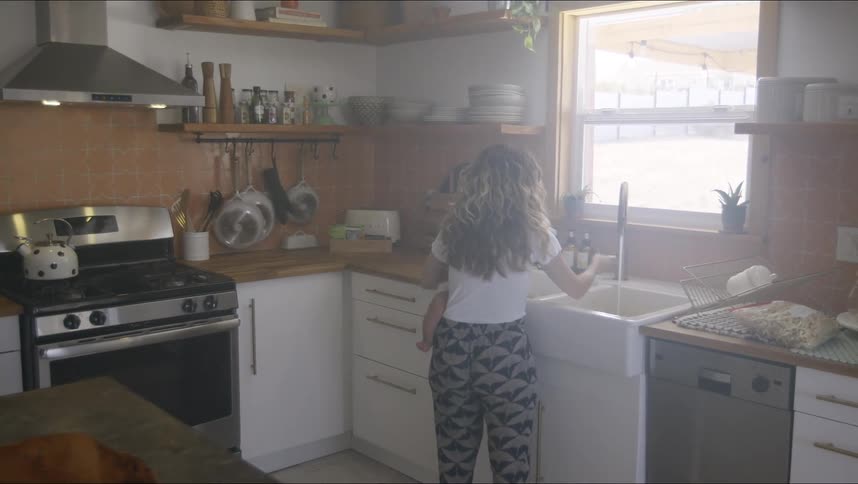 A woman carries a baby to the sink