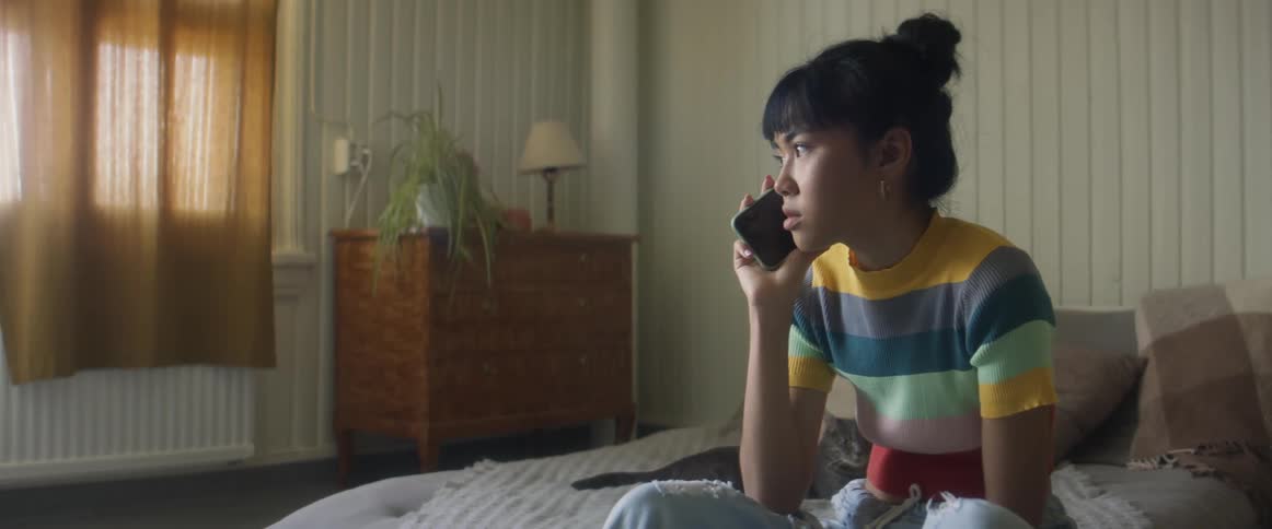 A woman is sitting on a bed and talking on a cellphone