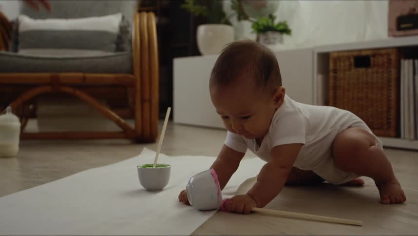 A woman hands bowls with green and pink paint in them to a baby