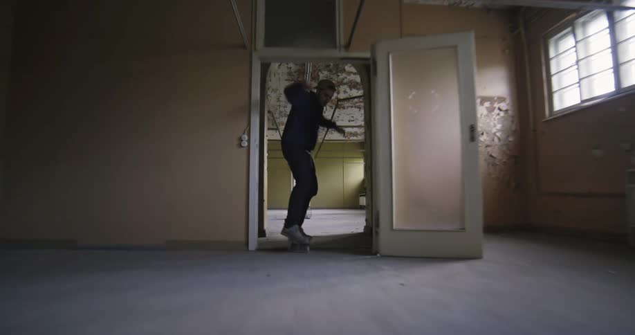 A skateboarder jumps over a barrel as he rides through an abandoned building