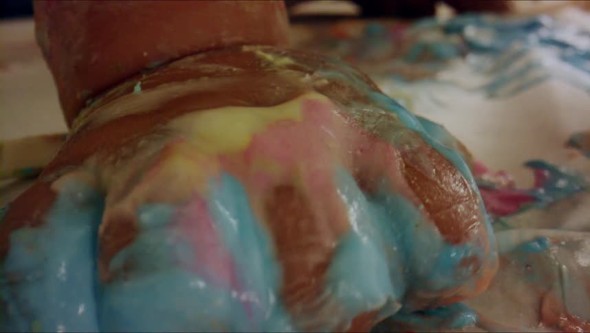 A baby with their hand covered in paint squeezes and makes a fist as they grab material