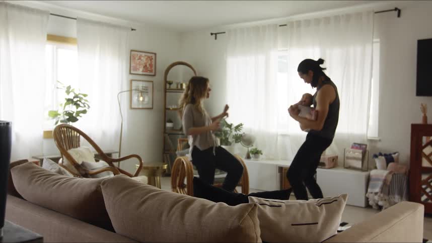 Man holds a baby as he and a woman dance around the living room