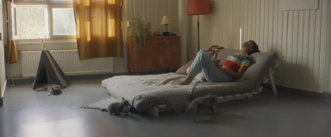 A young woman lays on her futon as kittens play around her