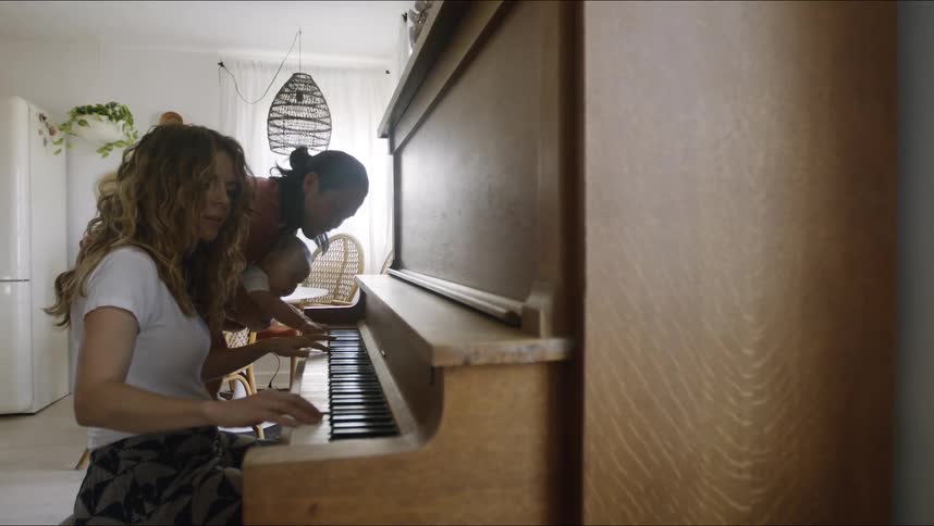 Father with long hair and red shirt plays piano next to mother with brown wavy hair and white t shirt