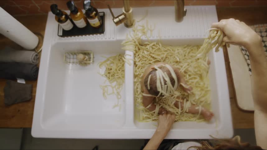 Overhead view of baby sitting in kitchen sink covered in noodles