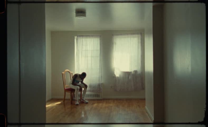 Black man walks across a room and sits on a chair looking sad and thoughtful