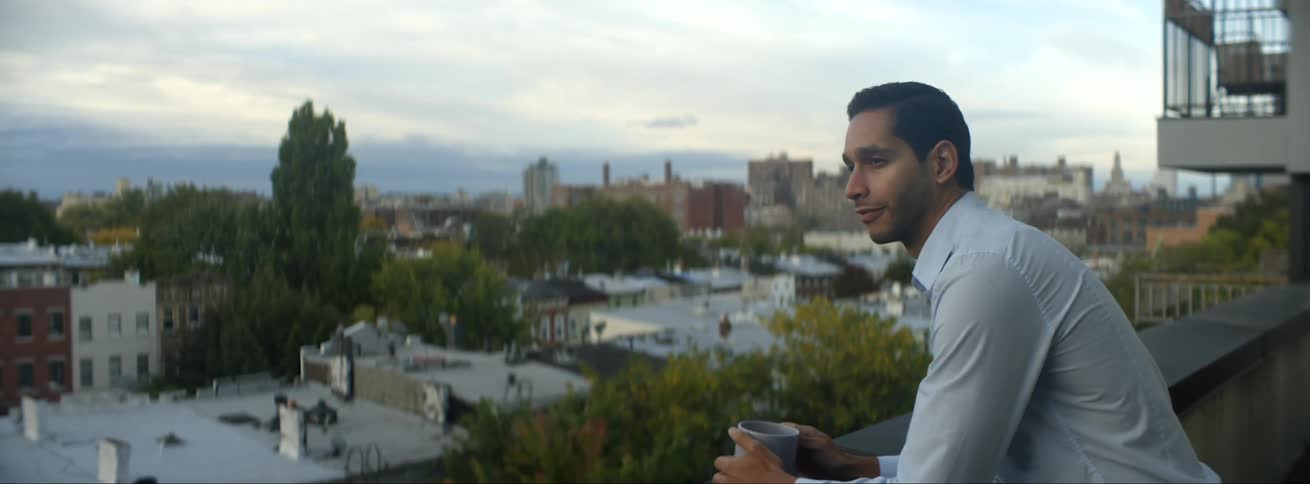 Man with blue shirt holds a cup standing on balcony