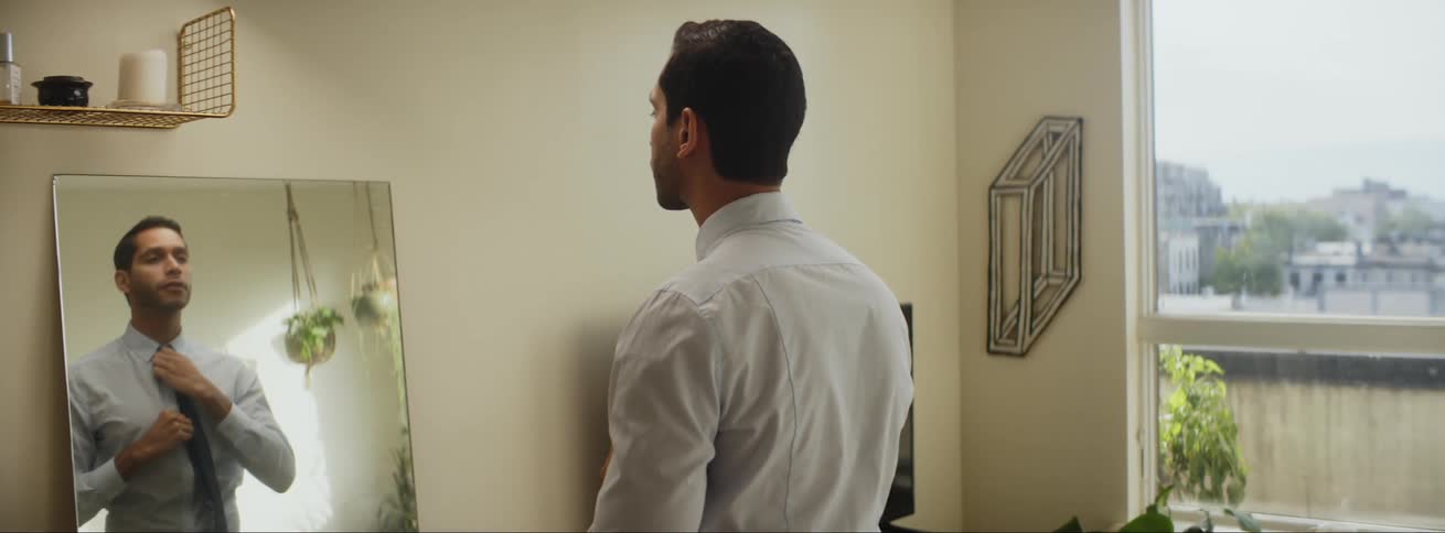 A man is standing in a mirror and putting on a tie