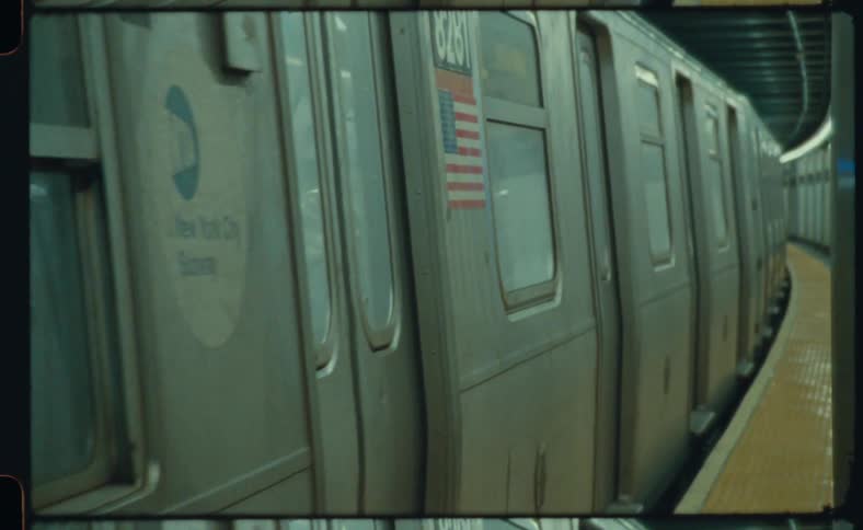 A subway train slows down and stops and then opens the doors and people get out