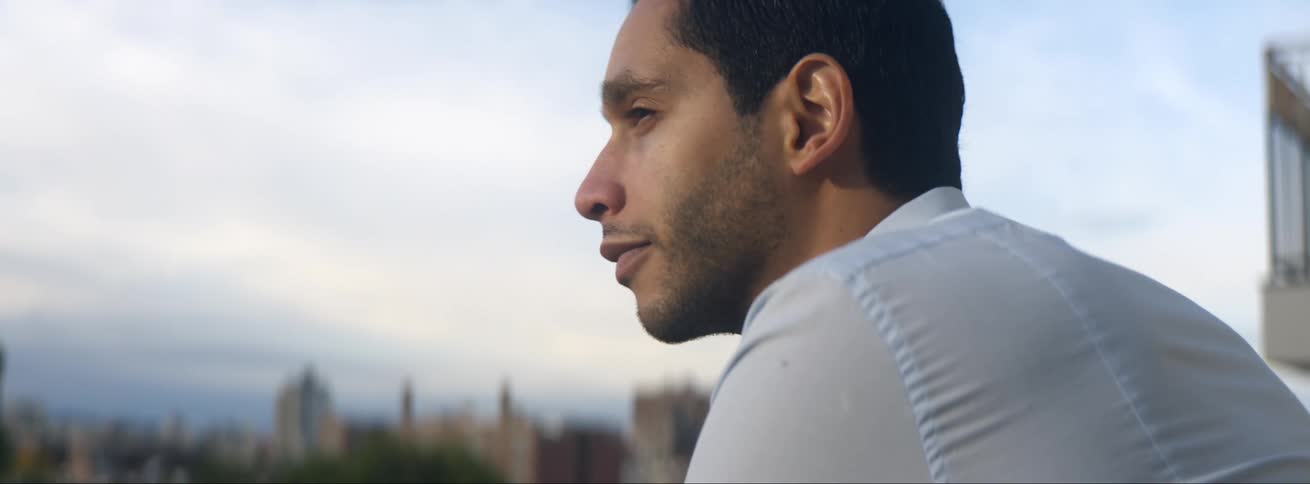 A man relaxes on his balcony with a cup of tea as he looks toward downtown