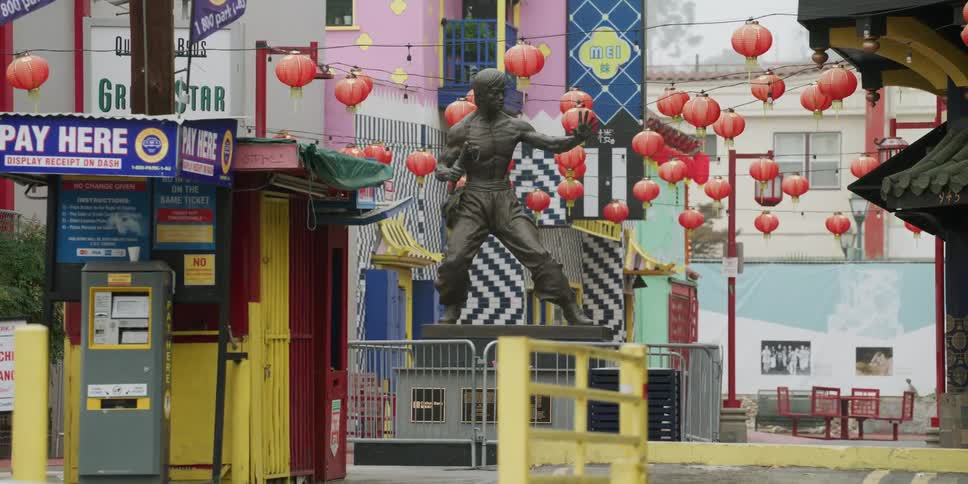 A man walks down a city street past a statue in front of a jazz club as cars drive past