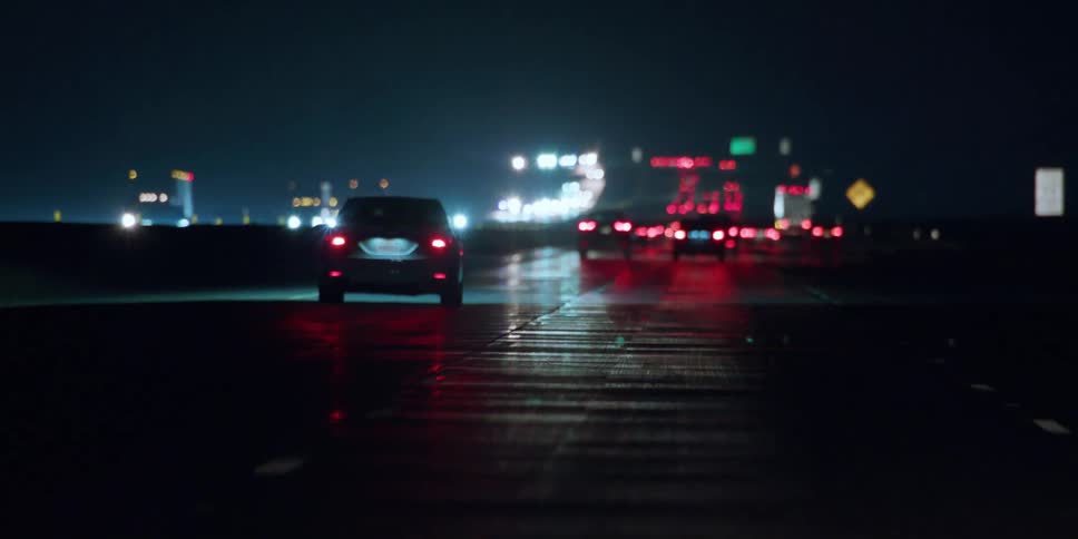 Busy traffic on a highway in the rain at night as car lights reflect on the wet road