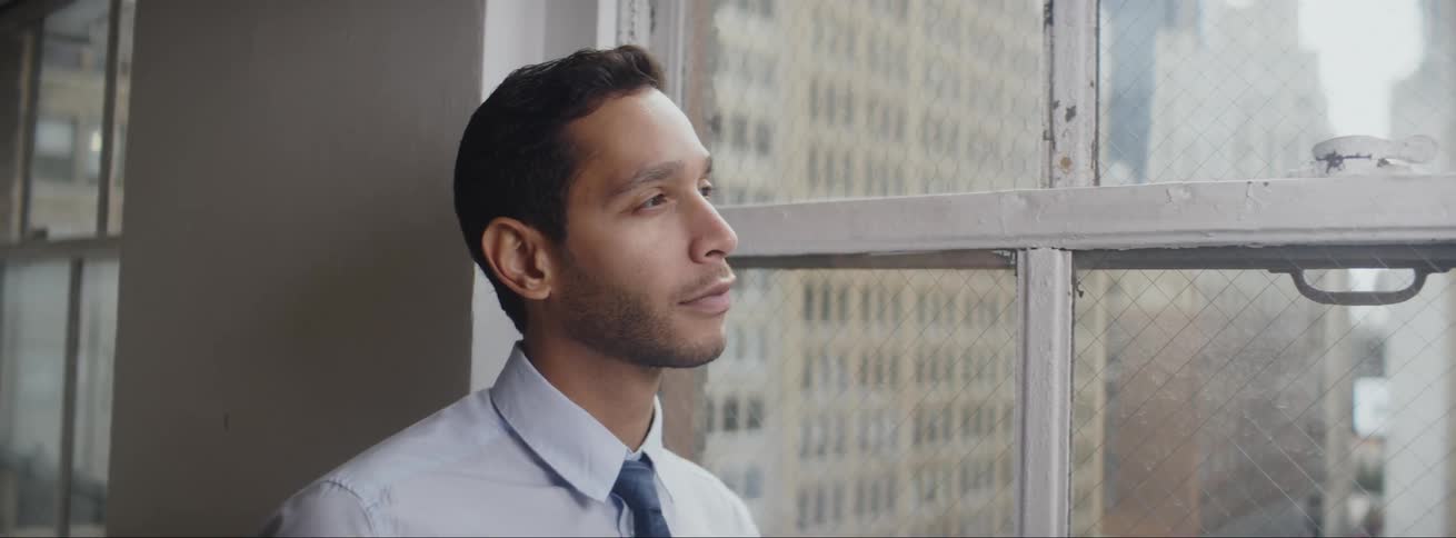 Businessman with shirt and tie looks out the office windows
