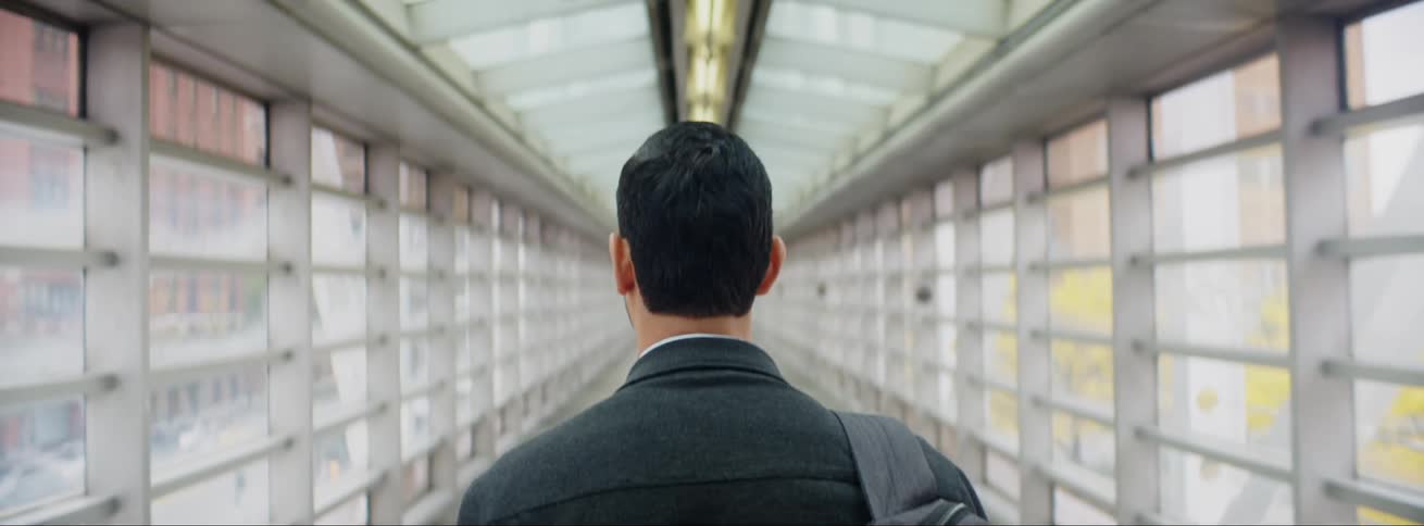 Man with a backpack over his shoulder walks through a corridor above the city traffic