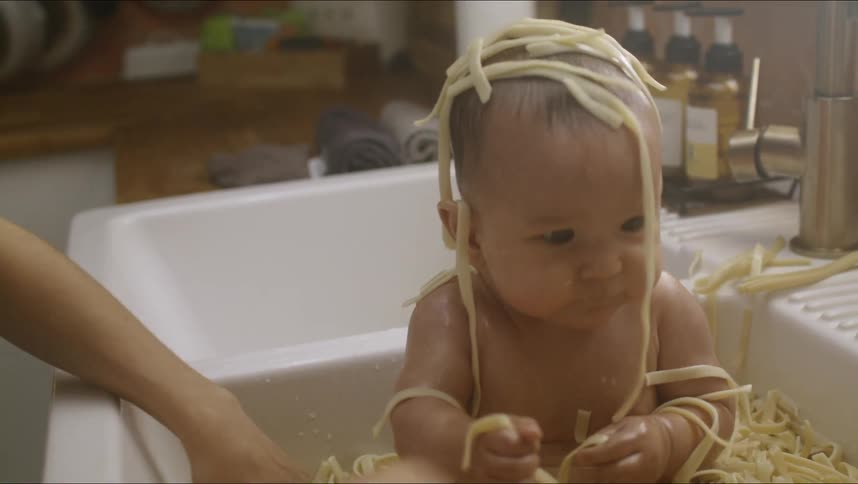 A baby is being bathed in a sink full of spaghetti