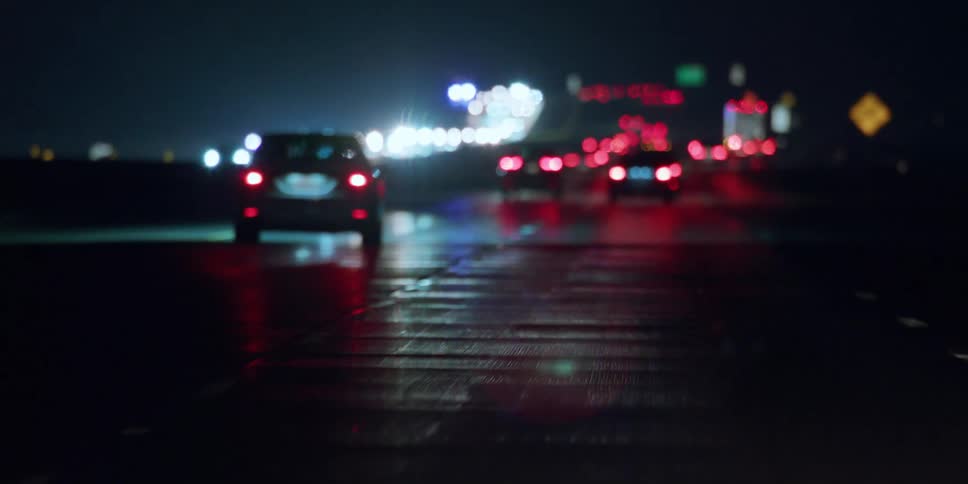 Busy traffic on a highway in the rain at night as car lights reflect on the wet road