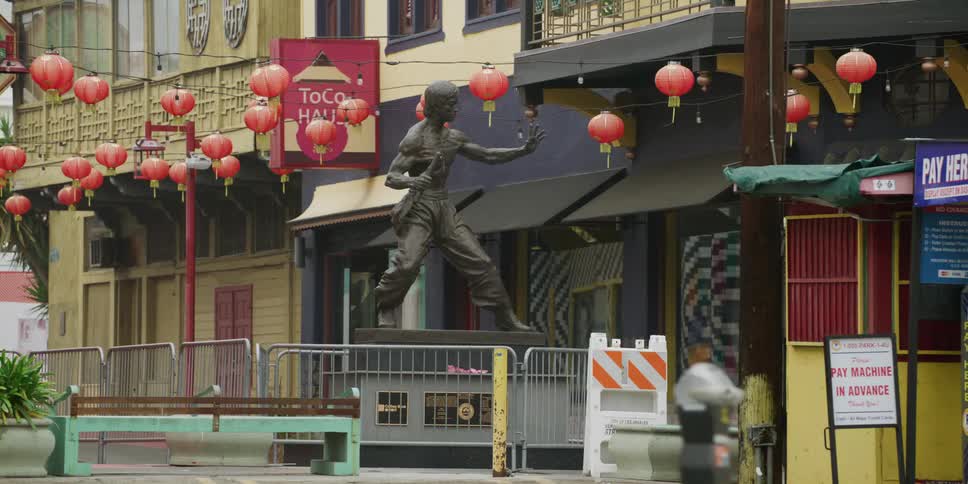Passing by a bronze statue of a martial artist in an asian market plaza in a citys downtown area in the daytime