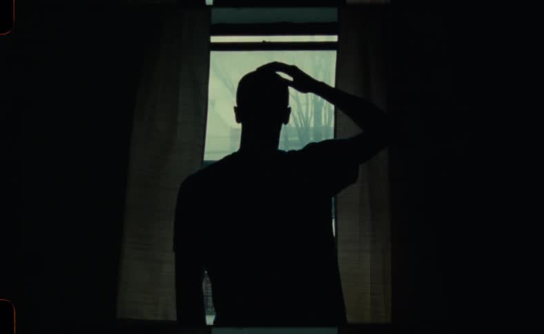 A man is walking towards his window indoors