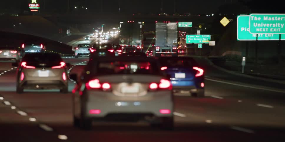 Dozens of vehicles travel a large highway at night