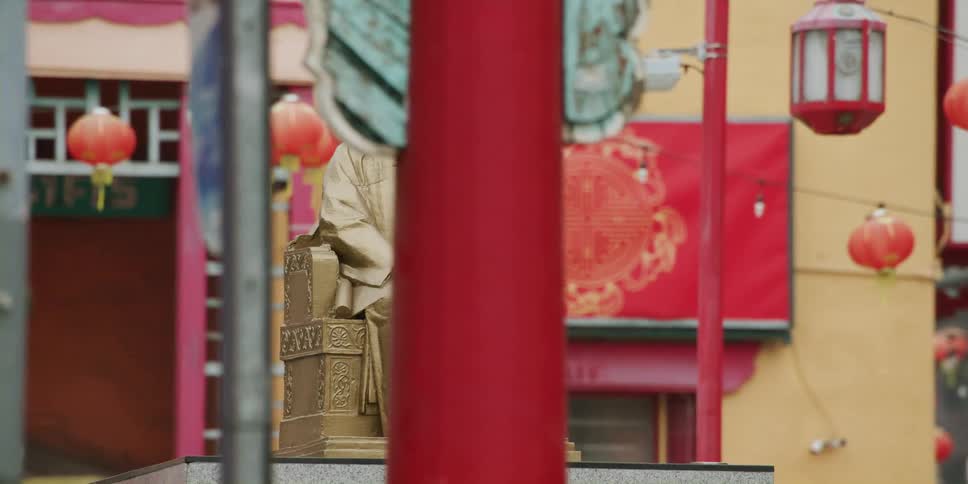 Statue sits on a pedestal in the city with hanging oriental lanterns nearby