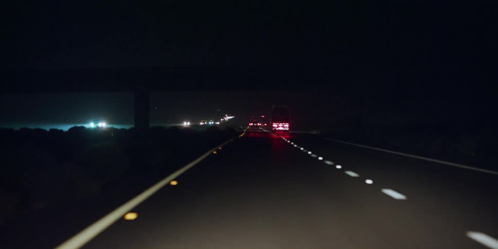 Automobiles travel on a road at night and the reflectors on the road shine in the darkness