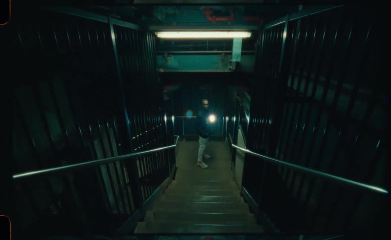 A man holds a flashlight at the bottom of a dark and empty stairwell